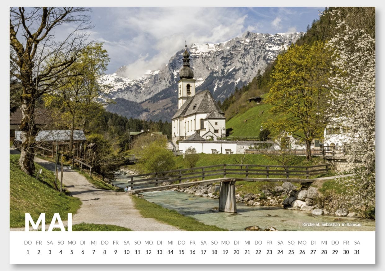 Ein malerischer Bergdorf mit einer weißen Kirche mit dunklem Turm, umgeben von grünen Bäumen und Bergen mit Schnee im Hintergrund, und einem Fluss, der durch die Landschaft fließt.