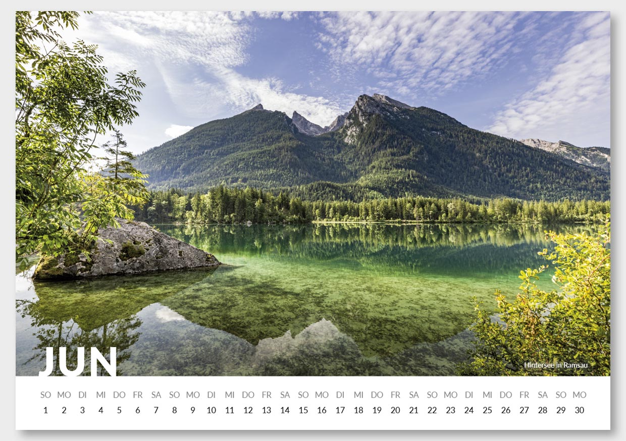 Kalenderblatt für Juni mit einem Landschaftsfoto des Hintersees in Ramsau, das einen ruhigen Bergsee mit klarem Wasser, umgeben von grünen Bäumen und hohen Bergen im Hintergrund zeigt, unter einem bewölkten Himmel.