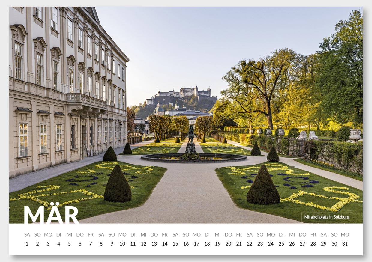Fotografie des Mirabellplatzes in Salzburg mit einem gepflegten Garten, bunten Blumen und Bäumen, im Hintergrund die Festung Hohensalzburg auf einem Hügel, bei Tageslicht.