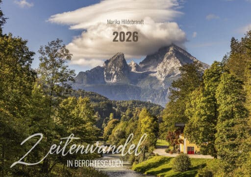 Berglandschaft mit hohen Bergen im Hintergrund, bewaldeten Hügeln und einem Haus am Fluss im Vordergrund, unter einem bewölkten Himmel, mit Text über die Landschaft, der den Namen "Zeitenwandel in Berchtesgaden 2026" und den Namen "Marika Hildebrandt" zeigt.